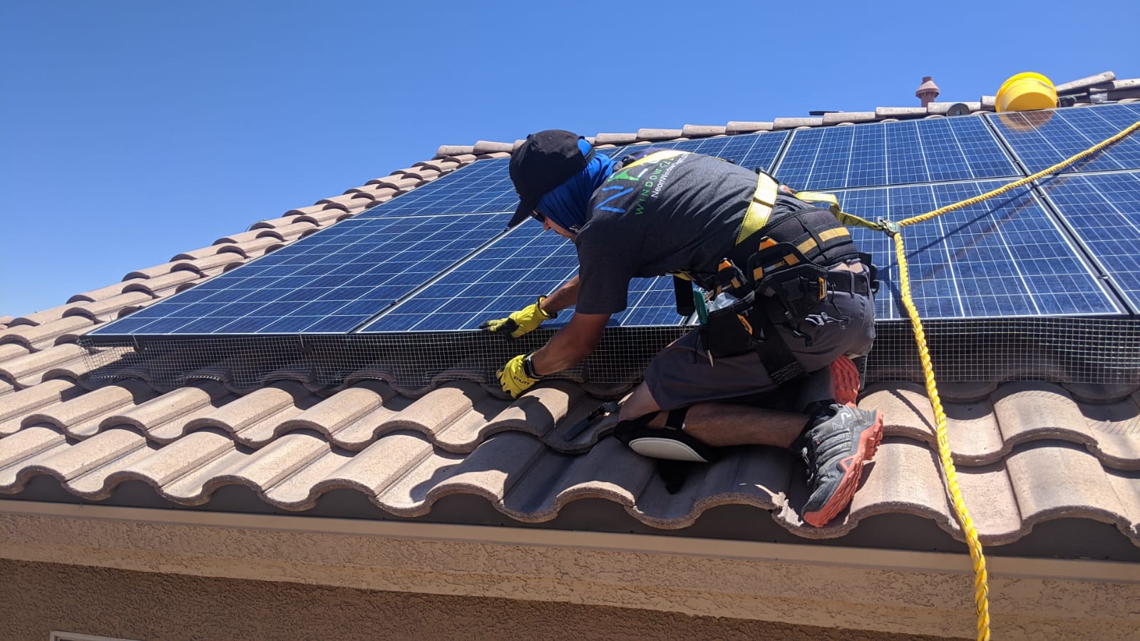 Neon Window Cleaning technician installing no-drill bird mesh around solar panels on a Las Vegas tile roof