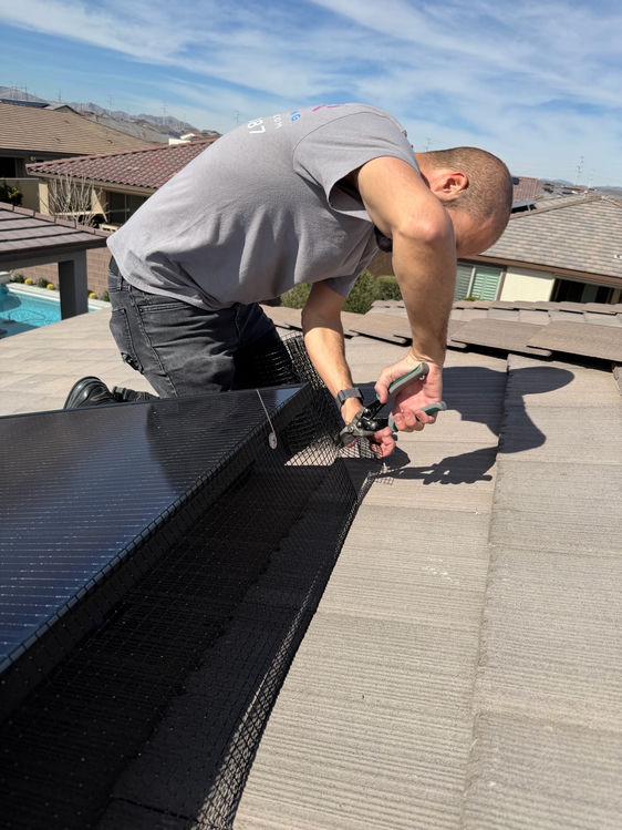 Technician fastening pigeon guard mesh clips to solar panel frames on a residential rooftop
